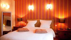 Habitación de hotel con pared a rayas, cama con sábanas blancas, dos lámparas de noche y un espejo en la pared izquierda.