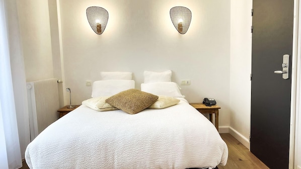 Un dormitorio con cama, dos luces fijadas a la pared, una mesita de noche con un teléfono y un radiador.