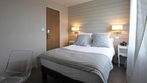 Una habitación de hotel con cama, mesitas de noche, una silla y una puerta.