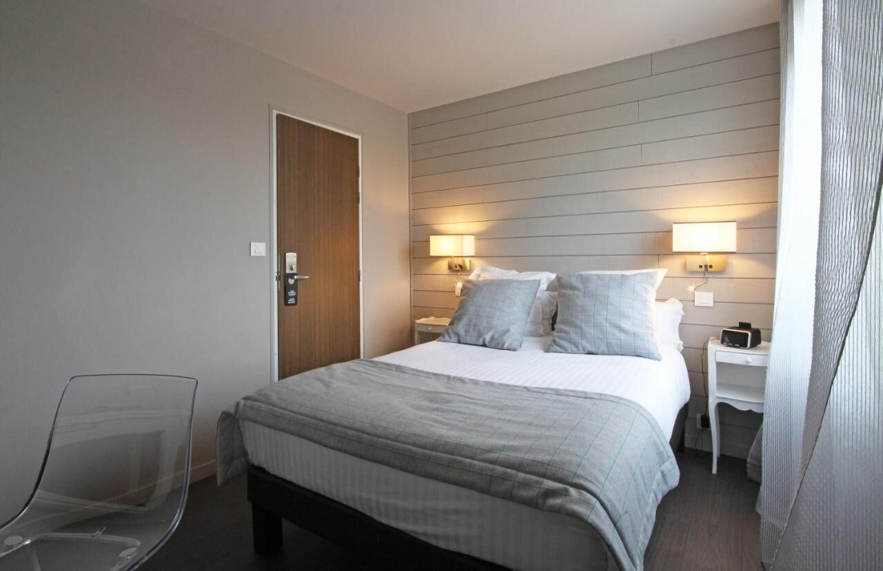 A hotel room with a bed, bedside tables, a chair, and a door.