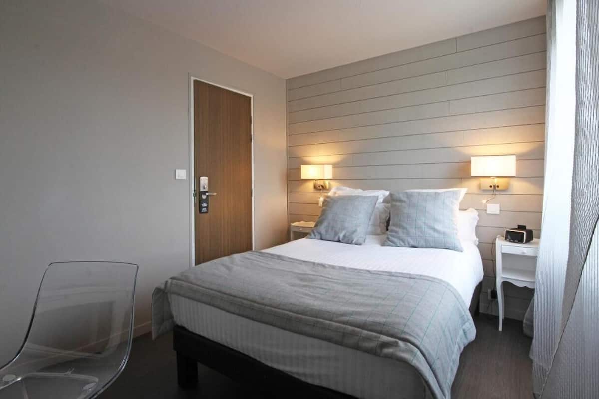 A hotel room with a bed, bedside tables, a chair, and a door.