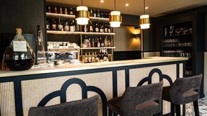 Un espace bar avec un long comptoir, des étagères remplies de bouteilles et des tabourets de bar.