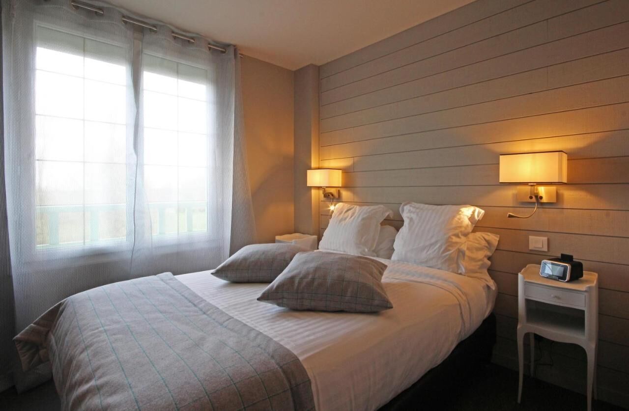A neatly made bed with two pillows, a bedside table with a clock, and two wall-mounted lamps.
