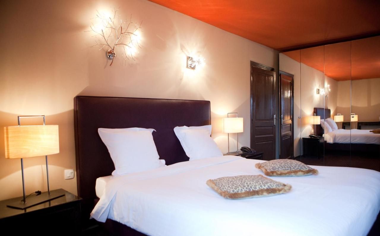 Ett hotellrum med en stor säng, två sängbord med lampor, en spegel och en väggmonterad lampa.
