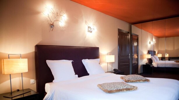 Habitación de hotel con una cama grande, dos mesitas de noche con lámparas, un espejo y una lámpara de pared.
