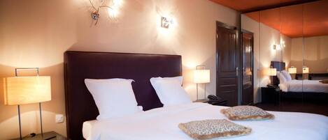 A hotel room with a large bed, two bedside tables with lamps, a mirror, and a wall-mounted light fixture.