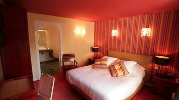 A hotel room with a large bed, two bedside lamps, a chair, a small table, and a door leading to a bathroom.
