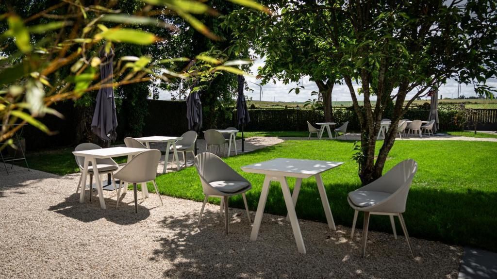An outdoor seating area with tables and chairs, surrounded by a well-maintained lawn and trees.