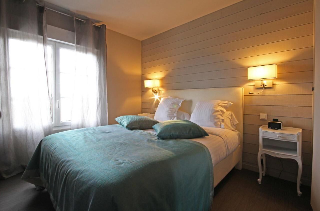 A bedroom with a bed, two bedside lamps, a nightstand, and a window with curtains.