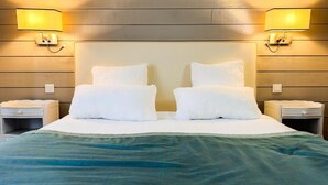 Una cama impecable con sábanas y almohadones blancos, flanqueada por dos mesitas de noche con lámparas, frente a una pared de madera.