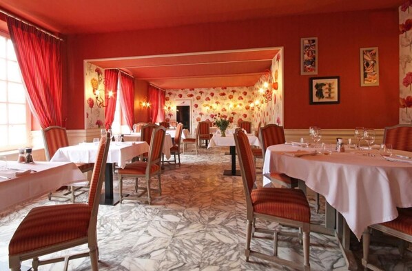 Comedor con mesas dispuestas para el servicio, cortinas rojas y papel tapiz floral.