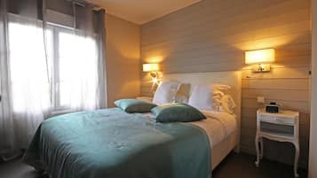 A bedroom with a bed, two bedside lamps, a nightstand, and a window with curtains.