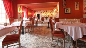 Comedor con mesas dispuestas para el servicio, cortinas rojas y papel tapiz floral.