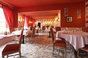 Comedor con mesas dispuestas para el servicio, cortinas rojas y papel tapiz floral.