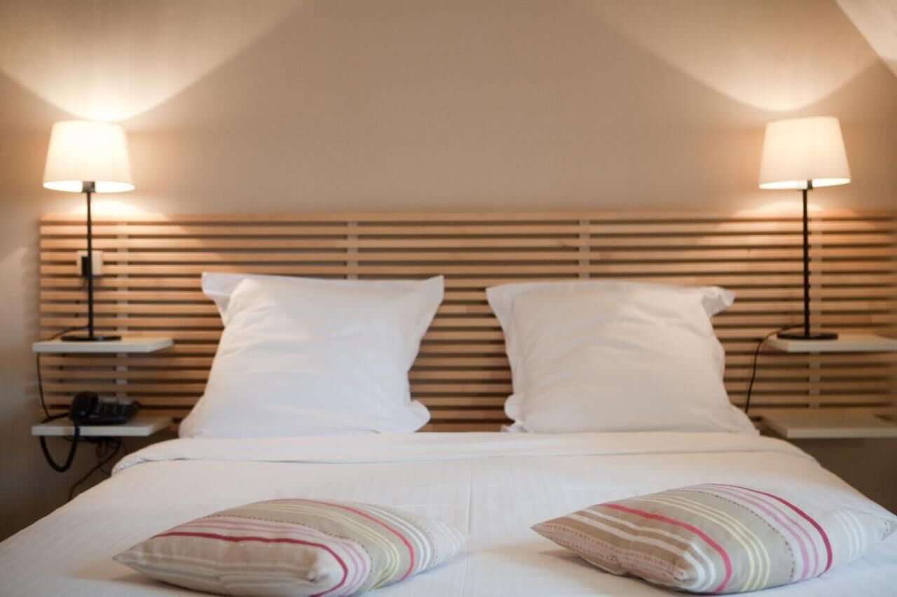 A hotel room with a bed, two bedside lamps, and a wooden headboard.
