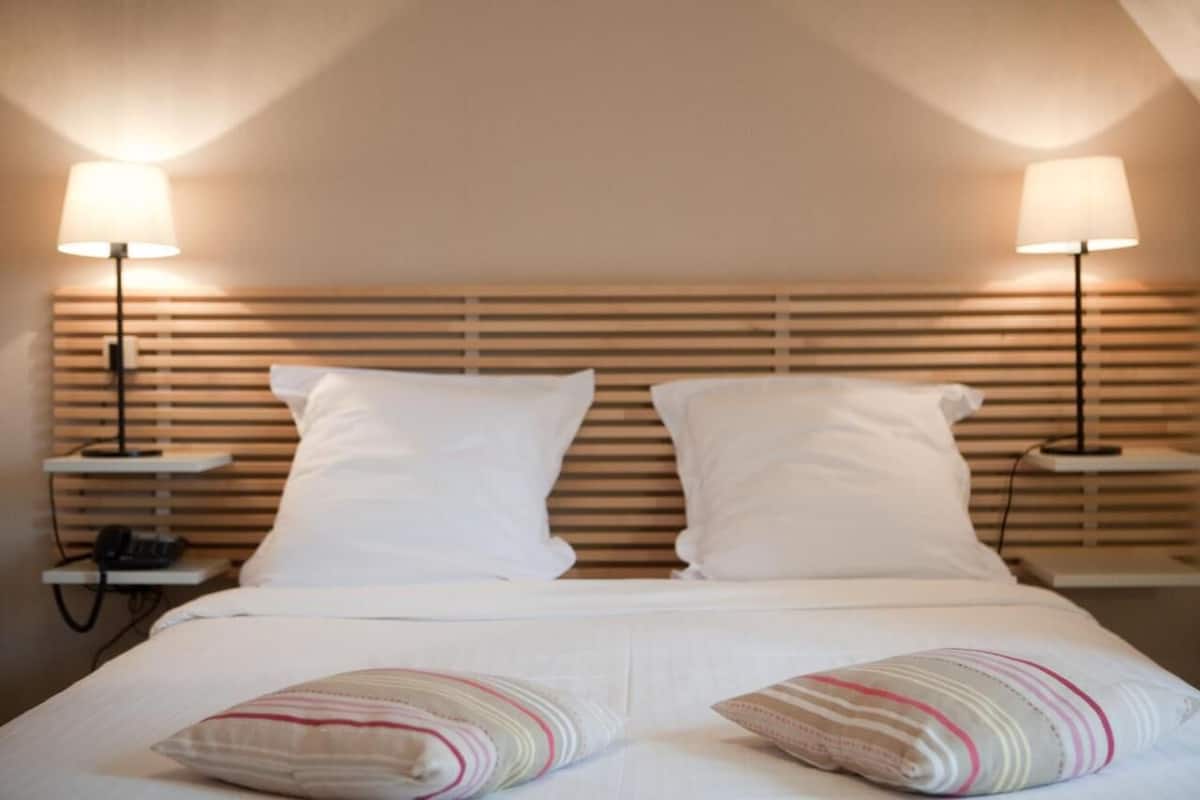 A hotel room with a bed, two bedside lamps, and a wooden headboard.