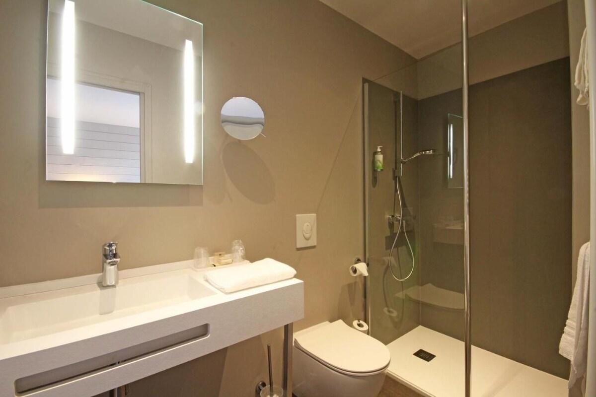 Un baño moderno con cabina de ducha de vidrio, un lavabo blanco y un inodoro.