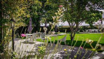 An outdoor patio area with tables and chairs, surrounded by greenery and trees.