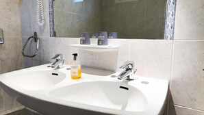Un baño con dos lavamanos, un espejo y artículos de aseo en un estante.