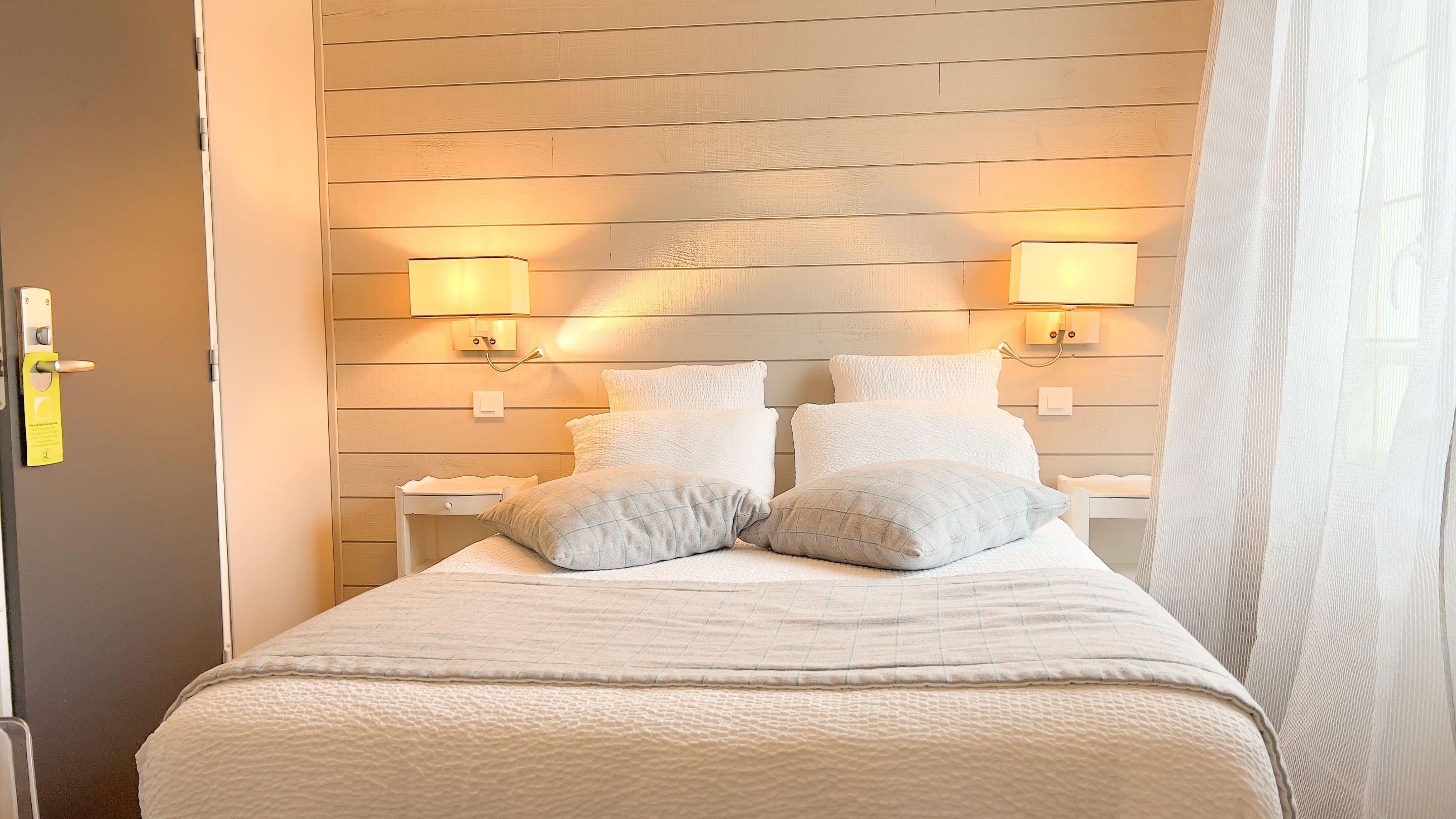 A neatly made bed with a quilted cover, two bedside tables with lamps, and a wooden wall paneling.