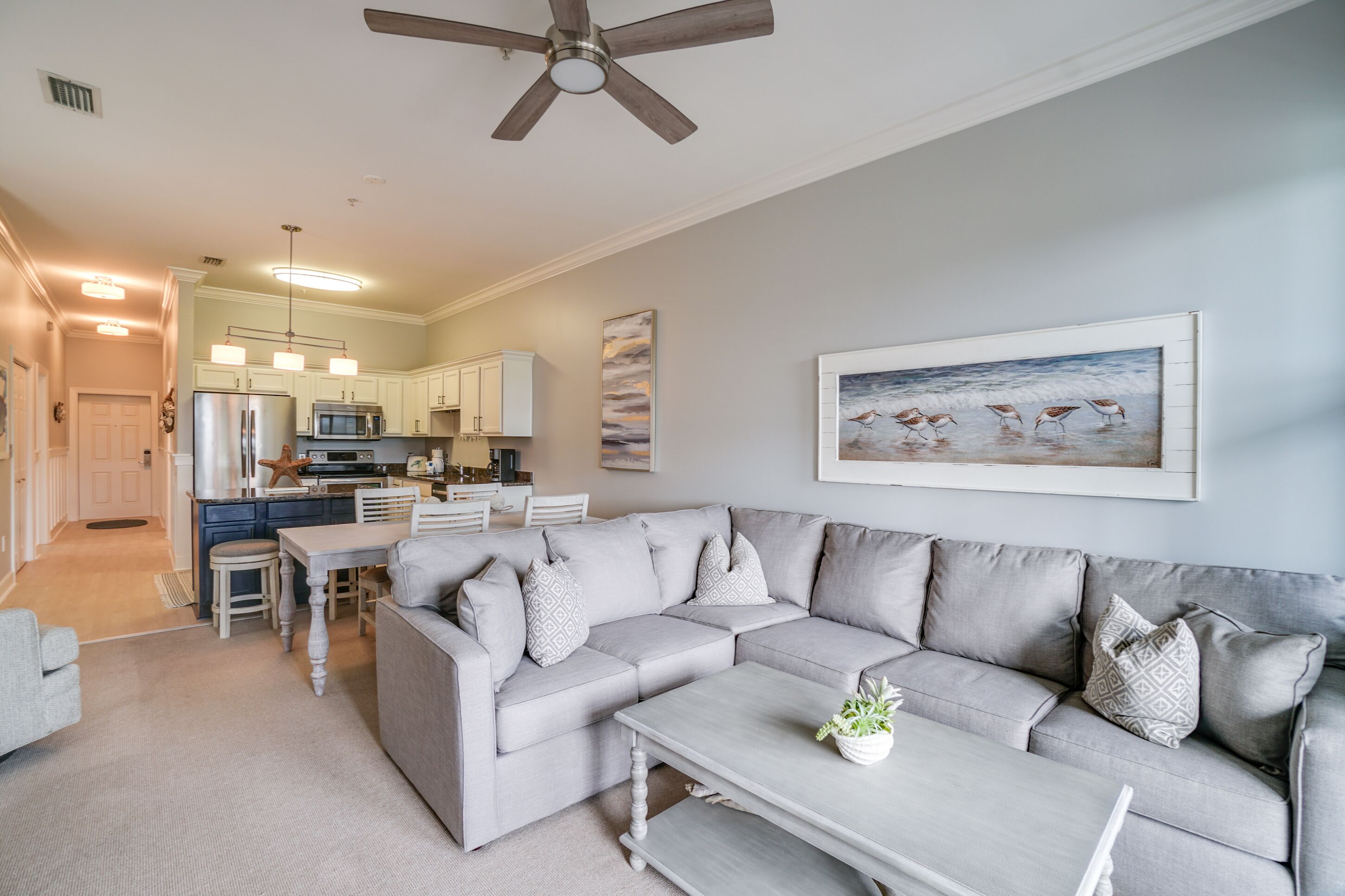 A modern living room with a sectional sofa, a dining table, and a kitchen in the background.