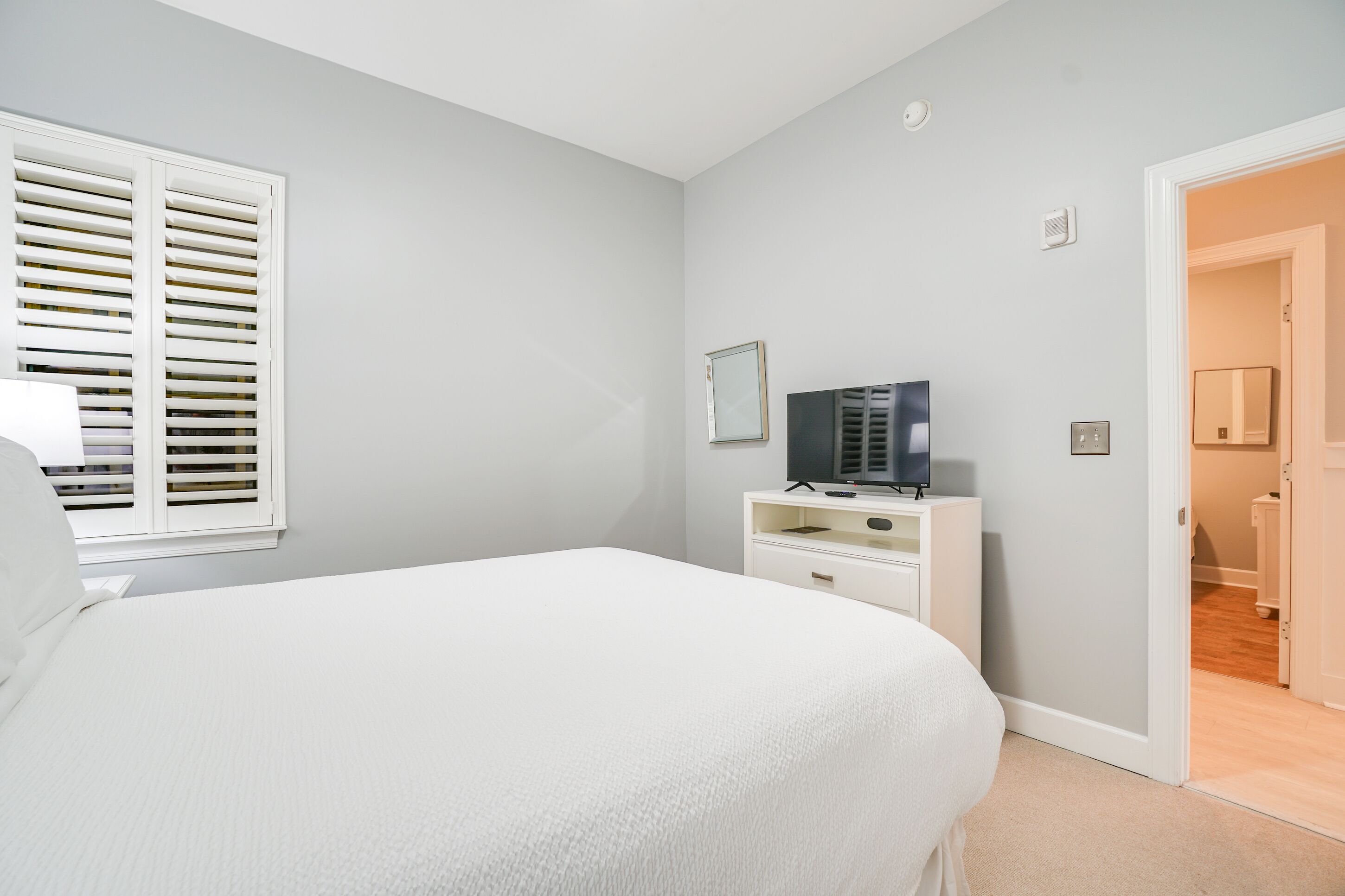 A bedroom with a bed, a TV on a white dresser, and a door leading to a bathroom.