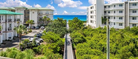 A coastal apartment complex with a view of the ocean, a parking area, and lush greenery.
