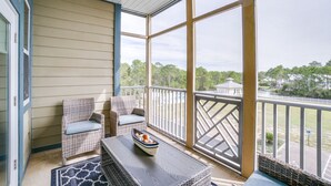 A covered porch with wicker furniture, a table with a bowl, and a view of trees and a building. - Seagrove Highlands By Panhandle Getaways (Santa Rosa Beach)