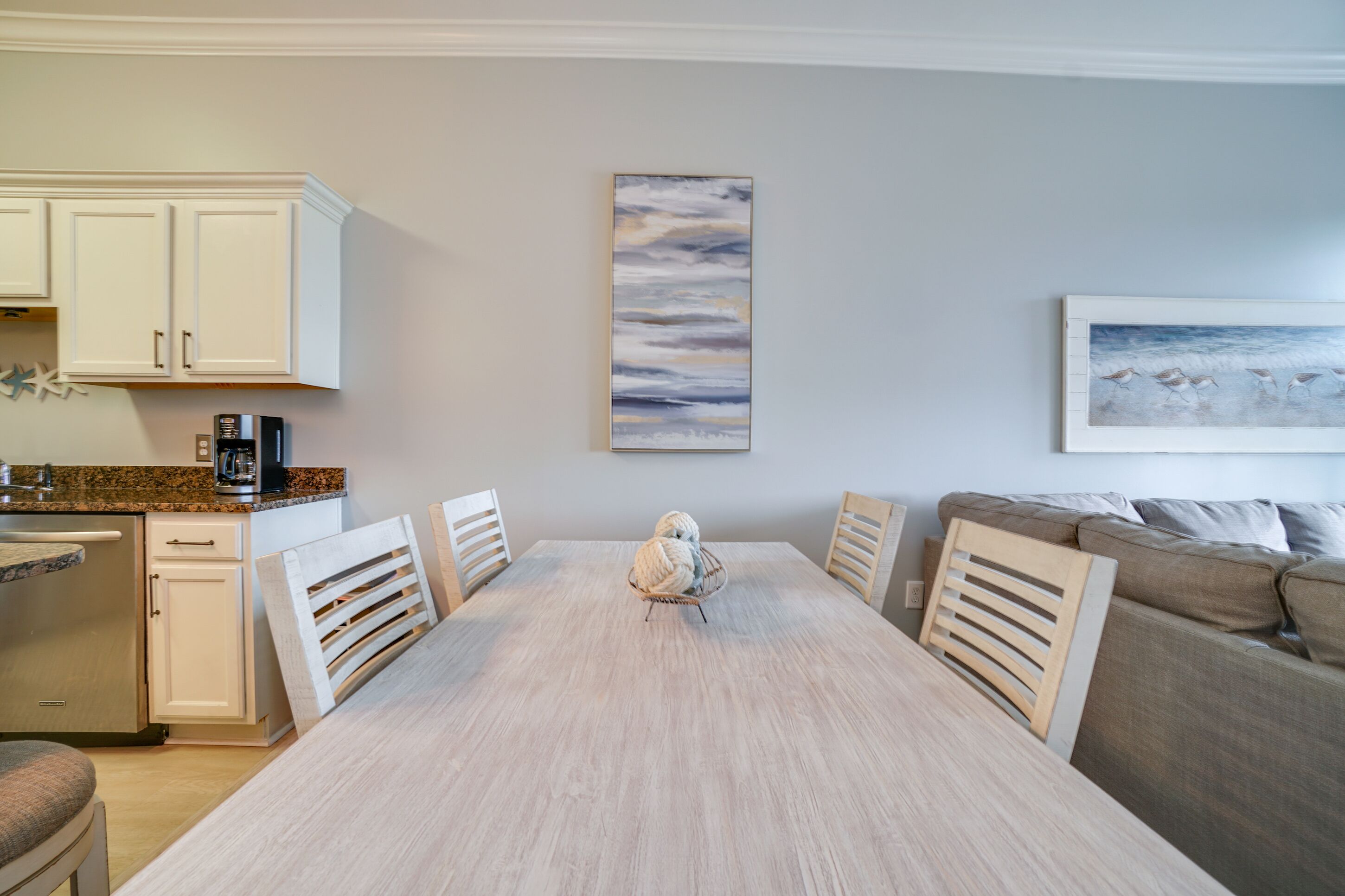 A dining area with a light wood table, white chairs, a white cabinet, and a painting of birds on the wall.