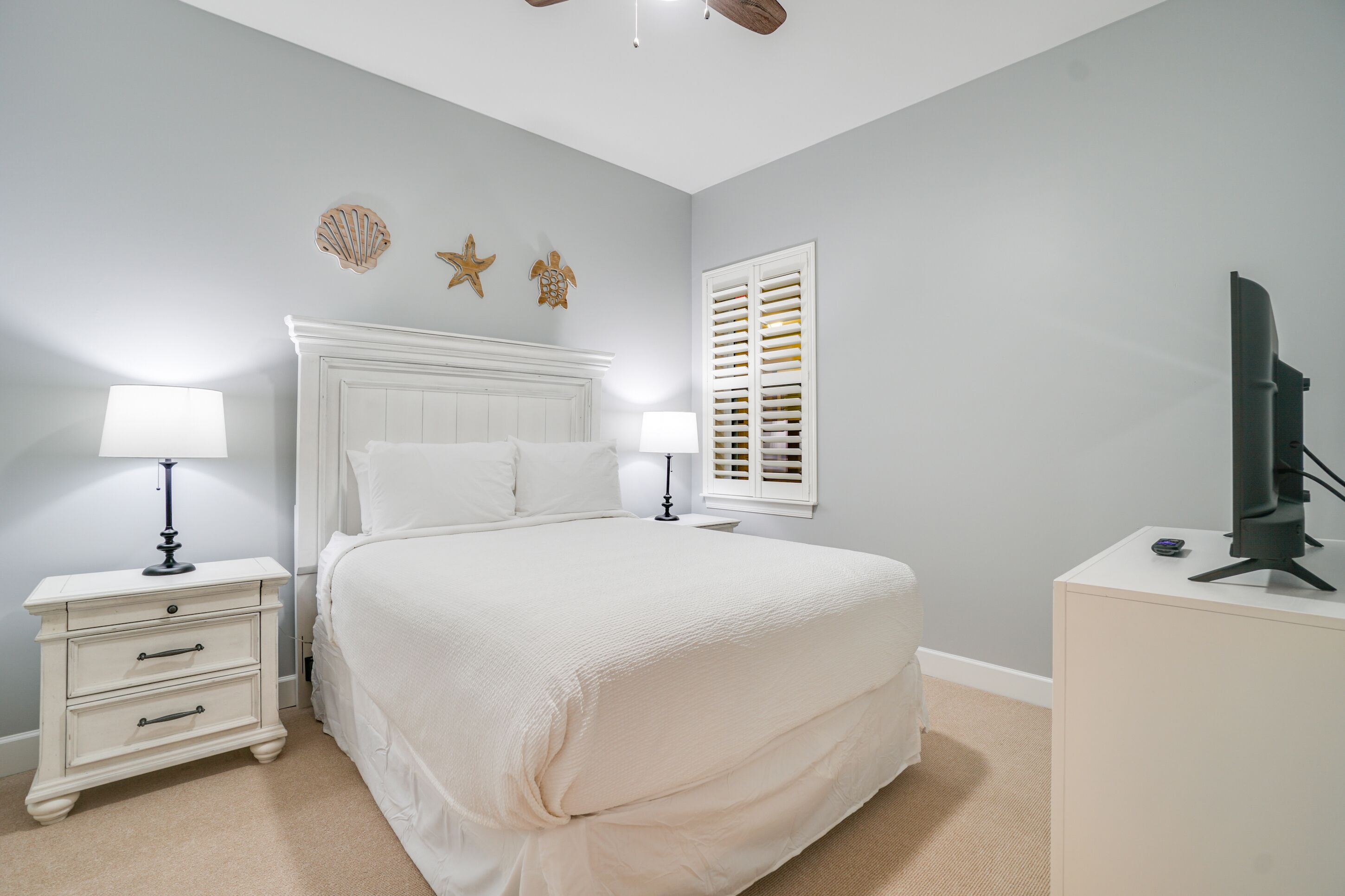 A bedroom with a bed, two bedside tables with lamps, a TV on a stand, and wall decorations.