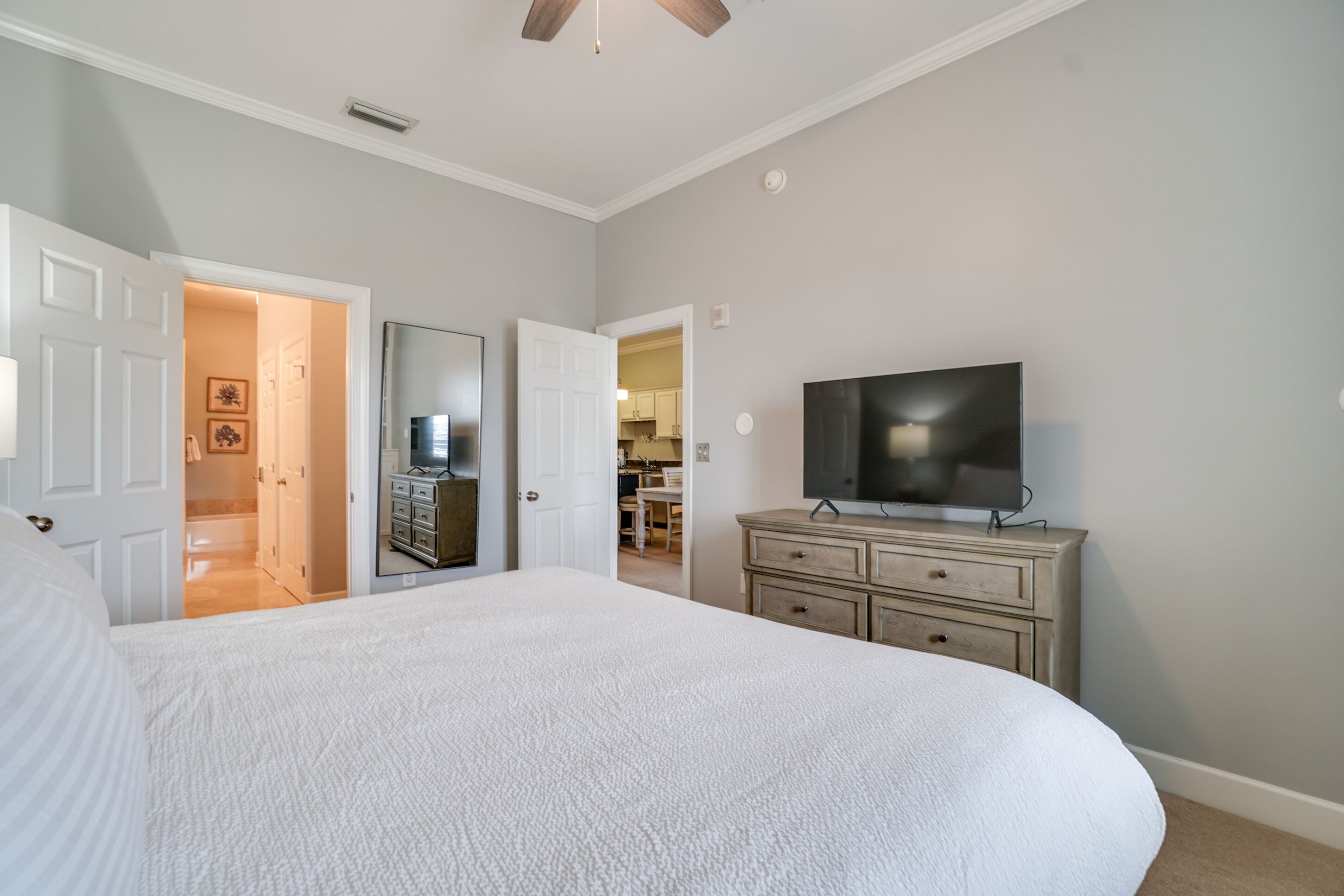 A bedroom with a large bed, a dresser, a television, and a ceiling fan.