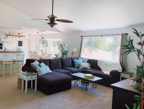 A modern living room with a sectional sofa, a small side table, a coffee table, and a dining area in the background.