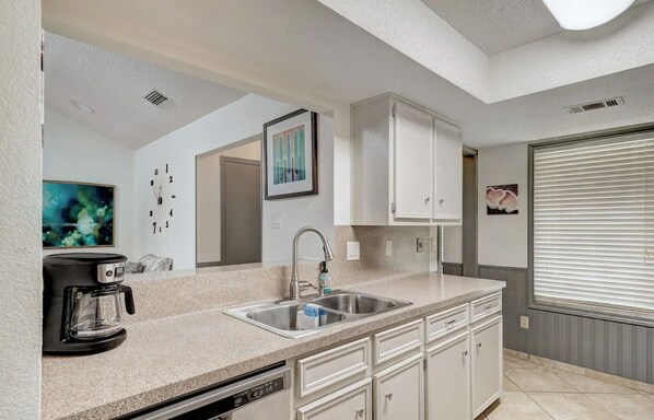 A modern kitchen with a built-in dishwasher, a coffee maker, a sink, and white cabinetry. - Hutto 4 BDRM GETAWAY HOME PERFECT FOR BUSINESS OR LEISURE. (Hutto)