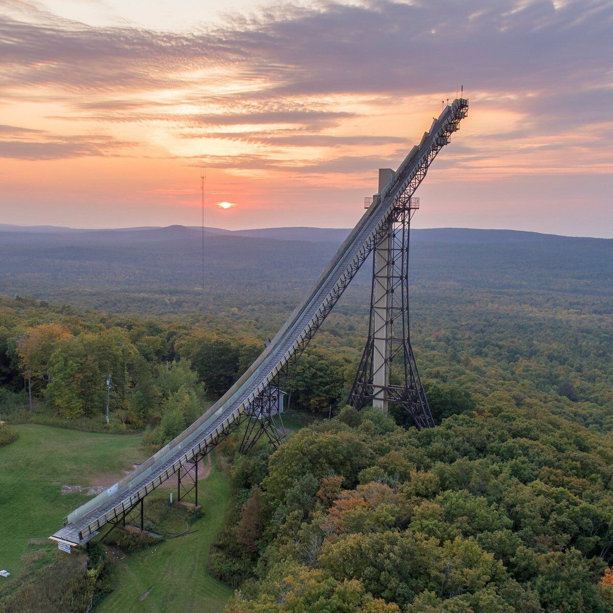 A large, steep metal structure in a forested area with a sunset in the background.
