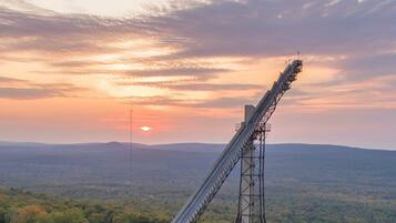 A large, steep metal structure in a forested area with a sunset in the background.