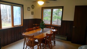 Ein Esszimmer mit Holztisch und -stühlen, einer kleinen Pflanze und Fenstern mit Blick auf Bäume.