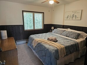 A bedroom with a bed, a bedside table, a lamp, a window, and a wall decoration. - Trail View 2: Private Hot Tub, Cold Plunge, Theater, Massage, Sauna, Mtn. Views (Bessemer)
