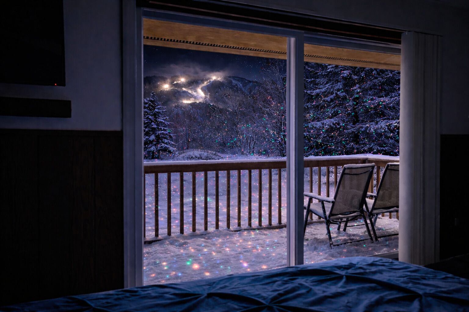 A room with a large window overlooking a snowy deck with chairs.