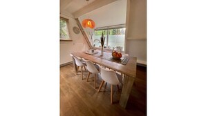 A dining area with a wooden table, white chairs, a basket of fruit, and a hanging light fixture.