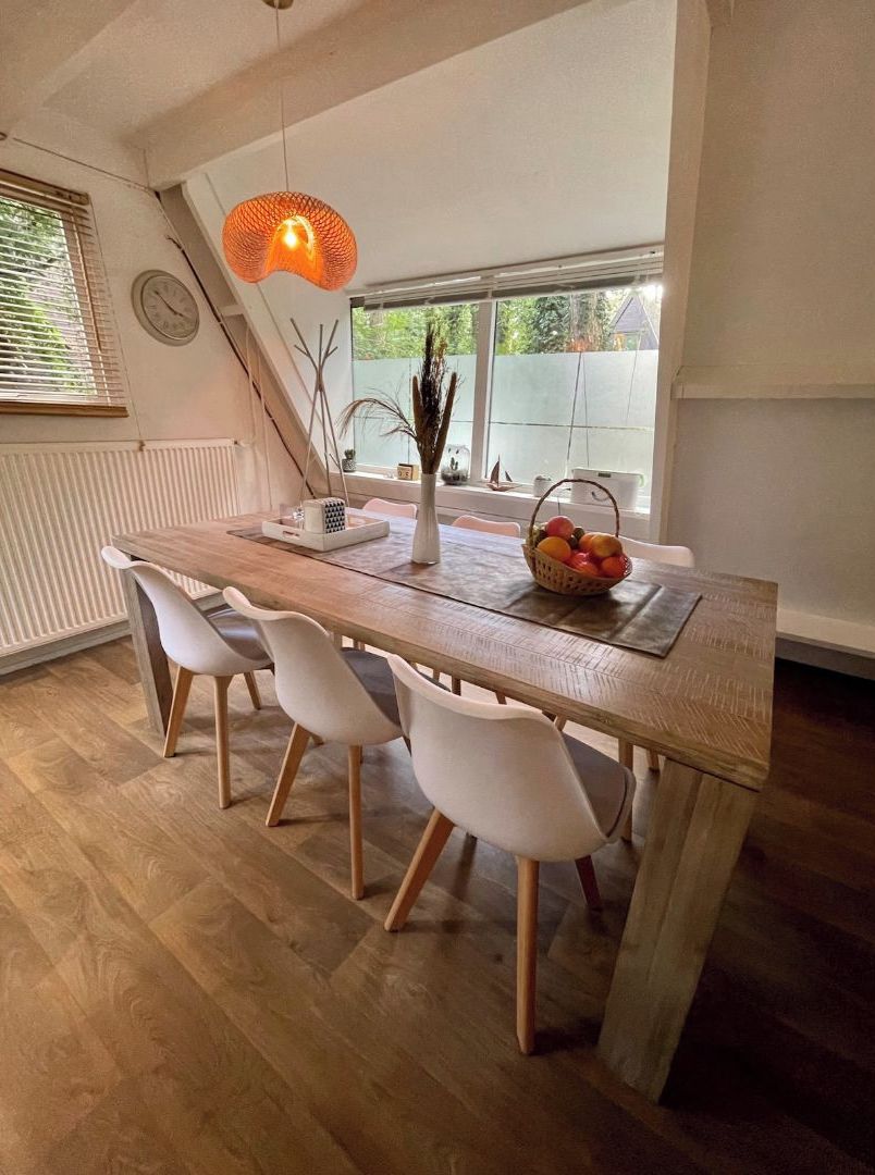Een eethoek met een houten tafel, witte stoelen, een mand met fruit en een hanglamp.