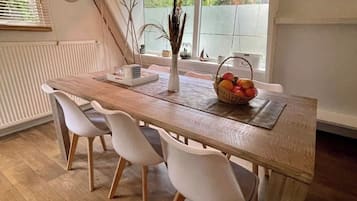 Een eethoek met een houten tafel, witte stoelen, een mand met fruit en een hanglamp.