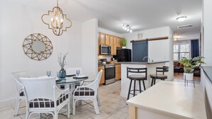 Een moderne keuken met witte kasten, een zwarte koelkast, en een eethoek met witte stoelen en een glazen tafel.