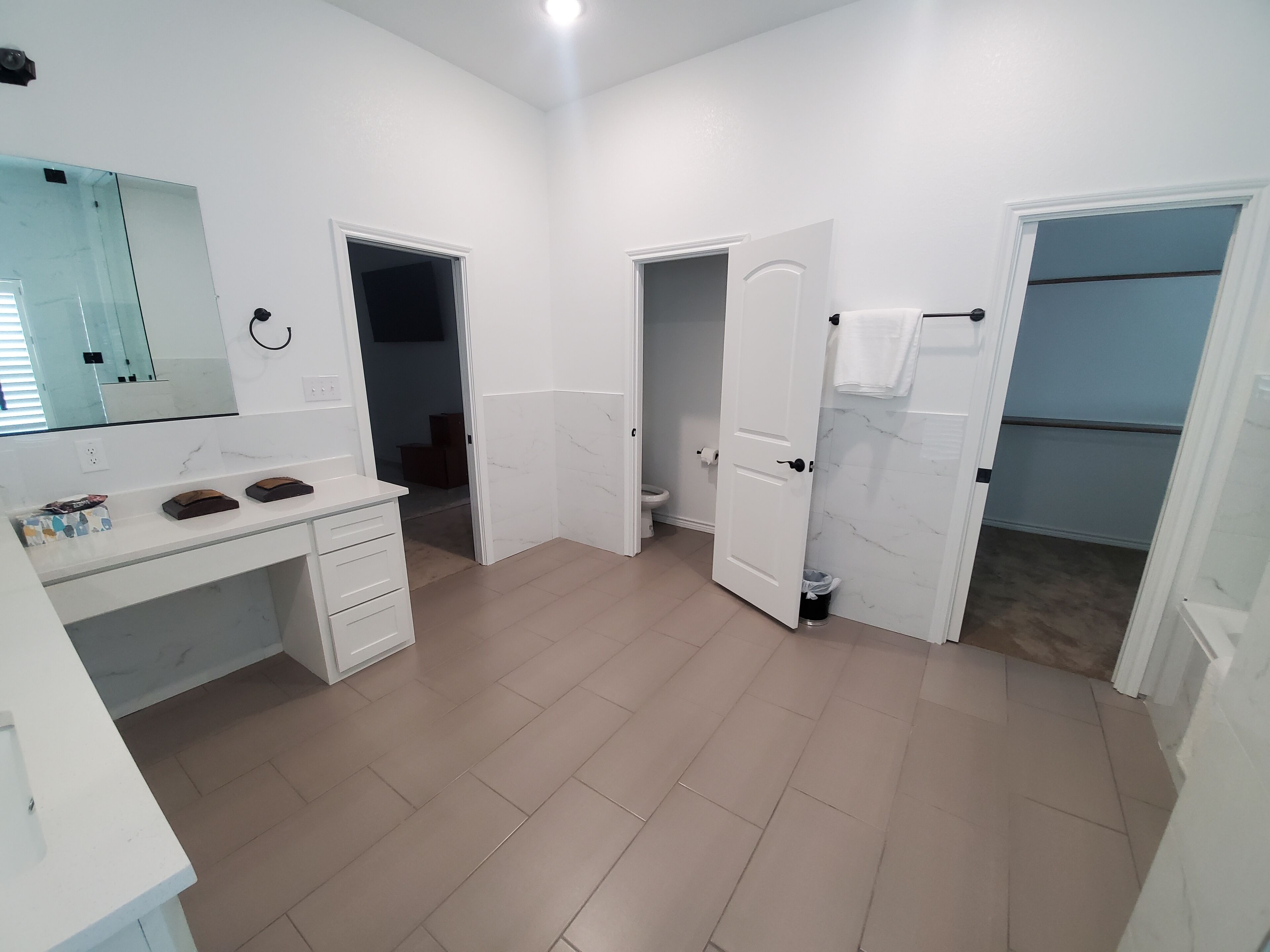 A spacious bathroom with a large mirror, a white vanity, a toilet, and a shower area.