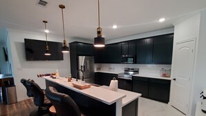 Een moderne keuken met donkere kastjes, roestvrijstalen apparatuur en een centraal eiland met barkrukken.