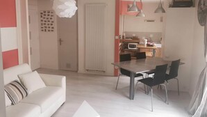 Ein modernes Wohnzimmer mit einer Couch, einem Esstisch und Stühlen. Im Hintergrund ist eine Küche zu sehen.