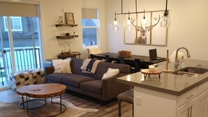 Une cuisine moderne avec un îlot central, un coin repas comprenant un canapé et une table basse, et un salon avec un divan et un tapis à motifs.