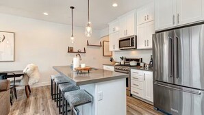 Une cuisine moderne avec des meubles blancs, des appareils en acier inoxydable et un îlot central doté de tabourets de bar.
