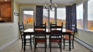A dining room with a table and chairs, a chandelier, and a view of autumn trees through large windows. - Beautiful 2BR/2BA Fall Line Condo with Mountain Views on Shuttle Route E2B (Killington)