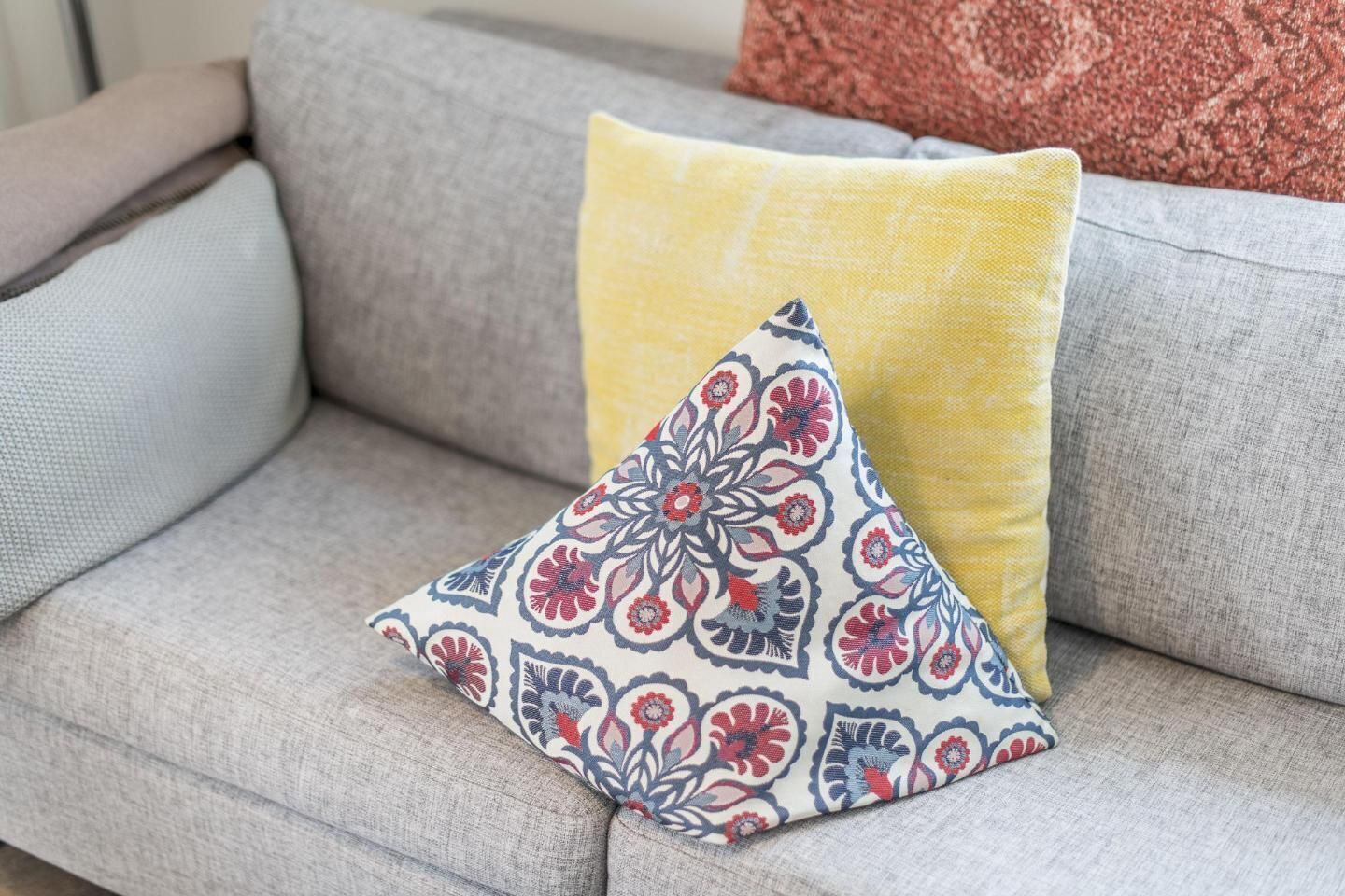 Un canapé gris avec deux coussins, l’un à motifs floraux et l’autre uni.