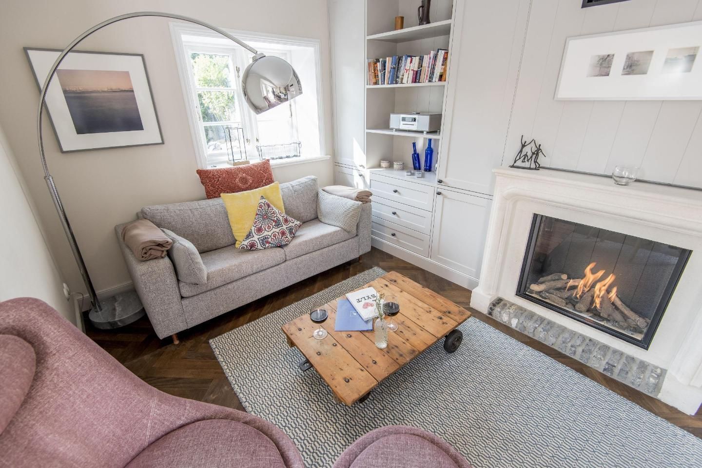 A living room with a sofa, coffee table, fireplace, bookshelf, and a window with a view.